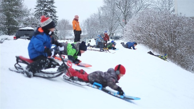 Des enfants s'apprêtent à descendre une pente, bien installés sur leurs toboggans.