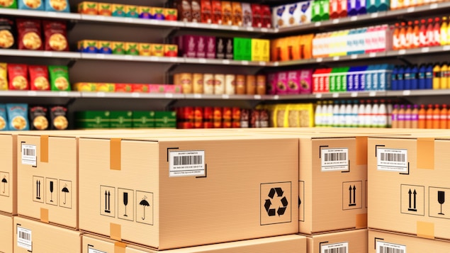 Des étagères d'épicerie remplies de produits devant lesquels sont déposées des boites de livraison en carton.