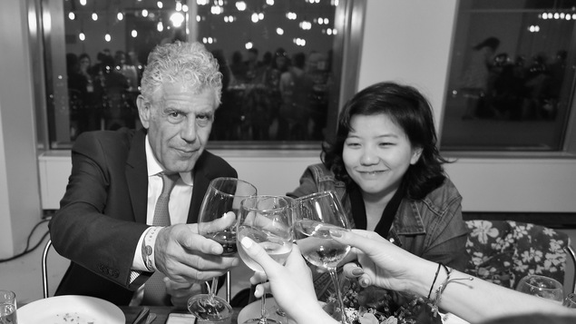 Une photo en noir et blanc d'Anthony Bourdain, qui regarde l'objectif de la caméra tout en portant en toast.