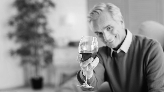 Un baby-boomer tend un verre de vin rouge vers la caméra.