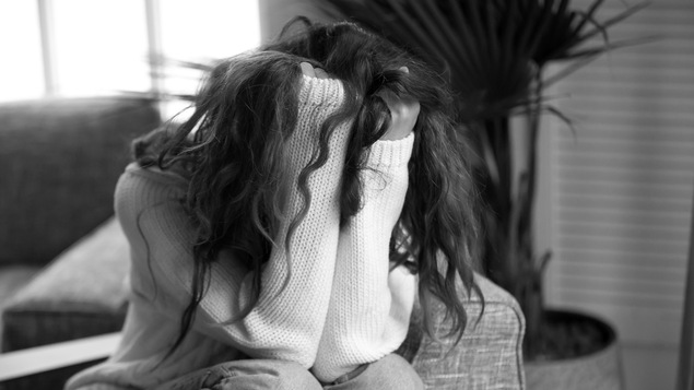 Une jeune femme assise sur le divan cache son visage dans ses mains.