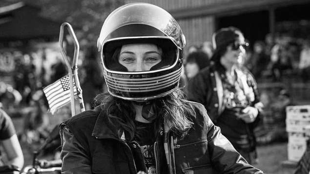 Photo en noir en blanc de la jeune femme, un casque de moto sur la tête et portant une veste de cuir.