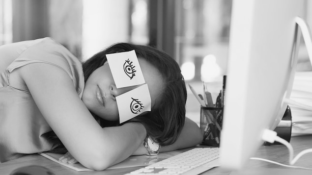 Une jeune femme a collé des cartons autocollants sur lesquels elle a dessiné des yeux, pour faire croire qu'elle est éveillée. Elle fait plutôt une sieste au bureau.