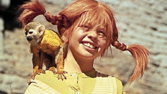 Une jeune fille rousse porte des tresses et a un petit singe sur l'épaule.