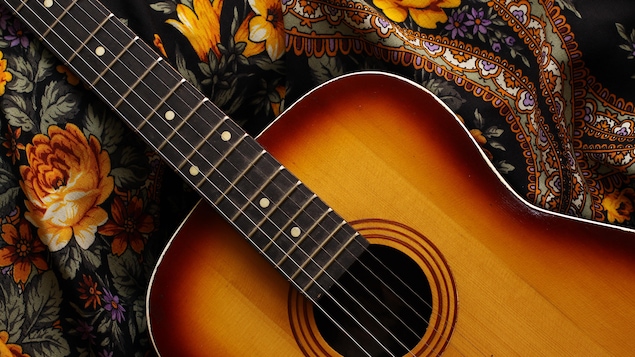 Une guitare acoustique en bois déposée sur un foulard fleuri rappelant le flamenco.