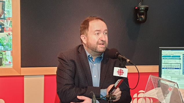 Un homme est photographié dans un studio de radio, devant un micro.