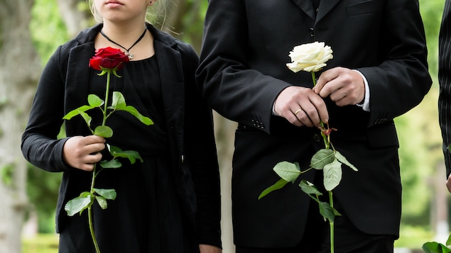 Une famille endeuillée sur un sentier se rend à des funérailles. Les deux enfants et les deux adultes tiennent tous une rose à la main. On ne voit pas leurs visages.