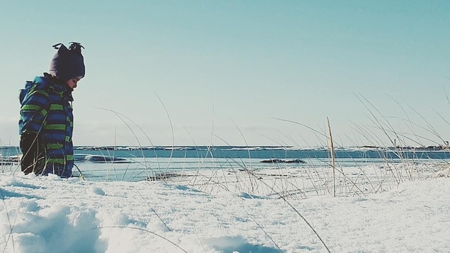 Un petit garçon regarde la plage enneigée à Natashquan.