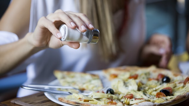 Une dame ajoute du sel à son repas.