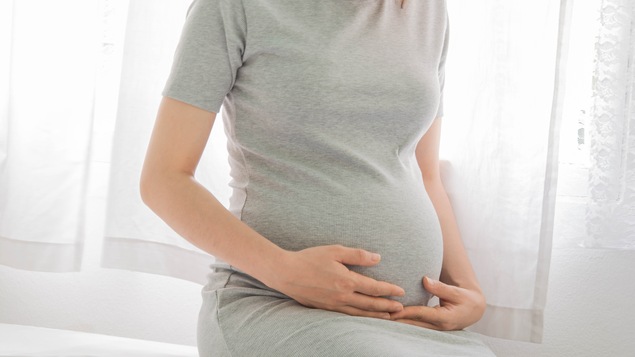 Gros plan sur le ventre d'une femme enceinte et les mains de celle-ci.