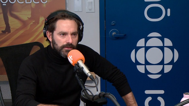 Guillaume Lemay-Thivierge au micro dans un studio radio présente la pièce de théâtre « Fais-toi une belle vie ».