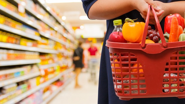 Une dame tient un panier de fruits et légumes dans une épicerie.