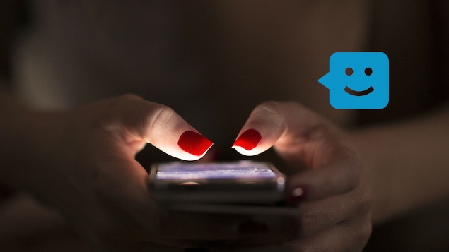 Un gros plan sur les mains d'une femme tenant un téléphone intelligent. Les ongles rouges de la femme sont éclairés par l'écran.