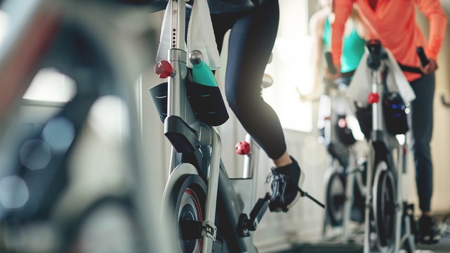 On voit des gens qui s'entraînent sur des vélos stationnaires. L'image est focalisée sur leurs jambes en action (on ne voit pas les visages).