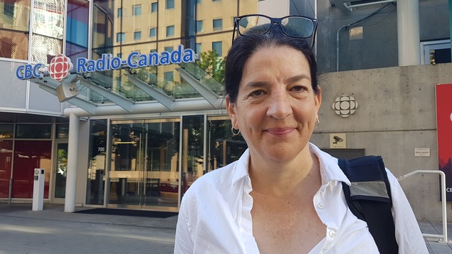 Une femme est photographiée plan taille devant l'édifice de Radio-Canada.