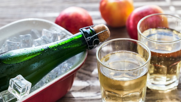 Une bouteille et deux verres de cidres sur une table en bois