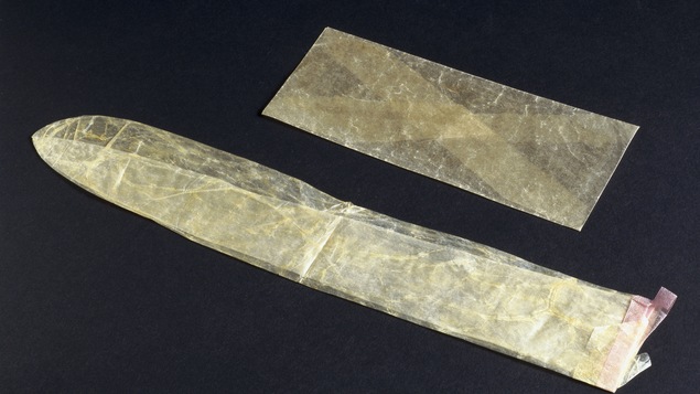 Un condom en lin est déposé sur une surface noire à côté d'une enveloppe.