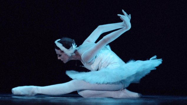 Une ballerine en costume exécute un mouvement sur le sol sur une scène.