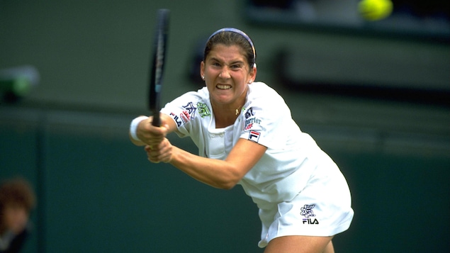 Une joueuse de tennis serre les dents avant de frapper avec sa raquette une balle qui arrive.