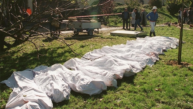 Photo prise à l'extérieur sur laquelle on voit plusieurs corps au sol recouverts de draps blancs.