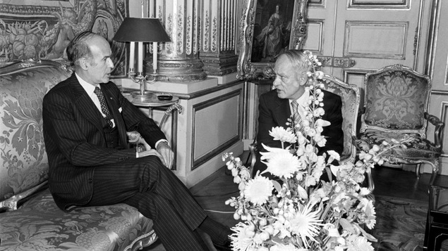 Photo en noir et blanc de deux hommes assis qui discutent.