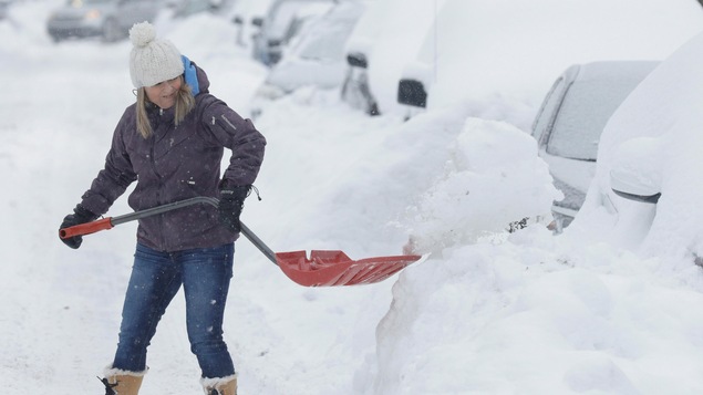 Une femme pellette la neige pour libérer sa voiture dans les rues de Montréal.