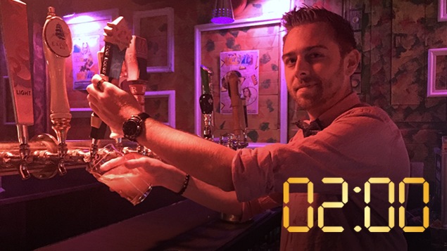 Un homme derrière un comptoir dans une boîte de nuit sert une bière pression.