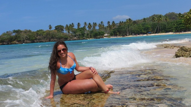 Une adolescente en maillot de bain est assise à la plage. Sa jambe droite est plus grosse que sa jambe gauche.