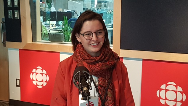 Une femme vêtue en rouge, est assise devant un micro dans un studio de radio.