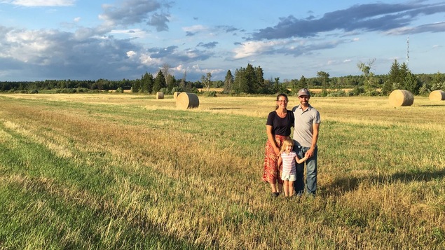 Le couple avec leur jeune fille se retrouve sur un champ, avec des rouleaux de foin en arrière-plan.