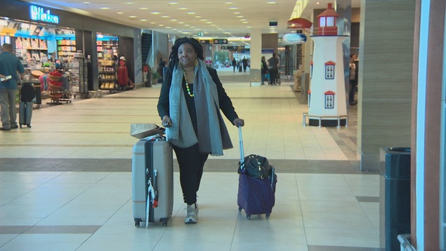 Jeanne Lehman marche dans un corridor d'aéroport, poussant ses deux valises.