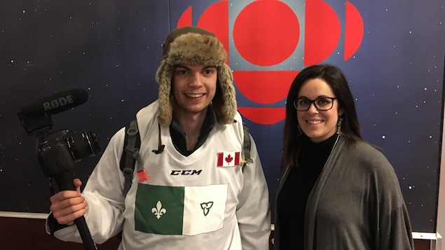 Un homme avec une caméra à la main pose en compagnie d'une femme devant le logo de Radio-Canada