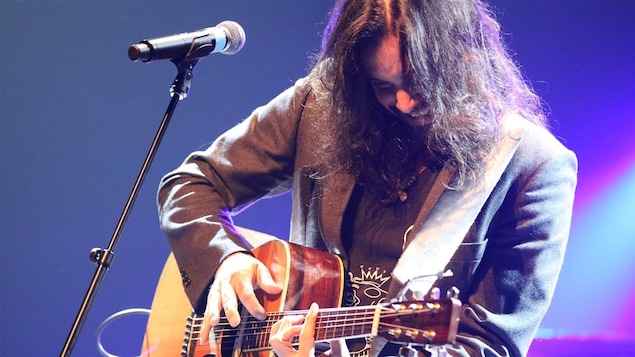 Le Franco-Manitobain Justin Lacroix chante sur scène en s'accompagnant à la guitare.