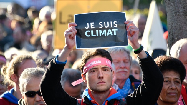 Homme dans une manifestation tenant une feuille où l'on peut lire : « je suis climat ».