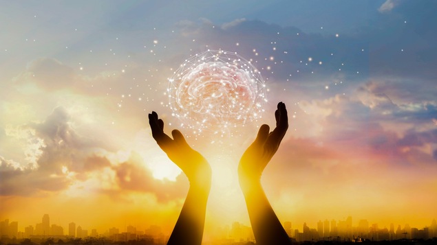 Deux mains tiennent un cerveau invisible devant un coucher de soleil.