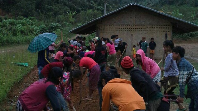 Des jeunes creusent dans la terre une rigole au Laos.