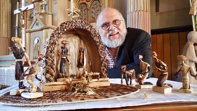 Un homme barbu prend la pose avec une crèche dans une église.