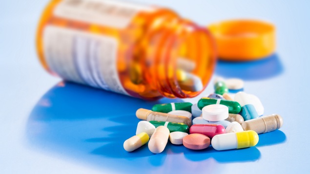 Des pilules de différentes couleurs à côté d'une bouteille de médicaments renversée.