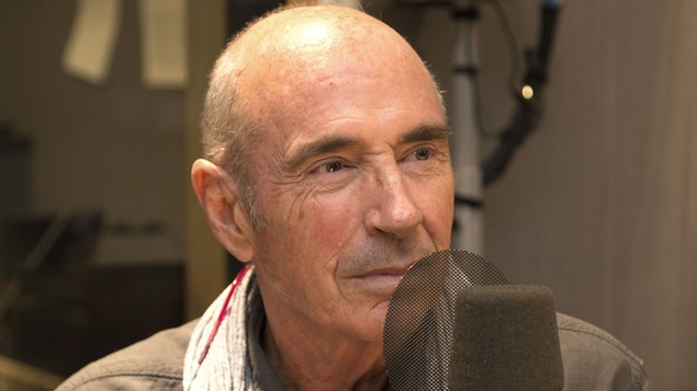 Lluis Llach est assis derrière un micro.