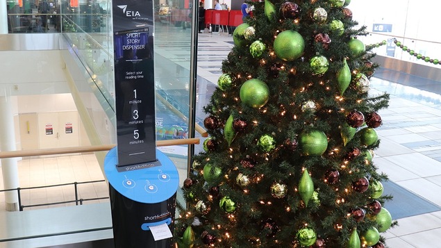 Une petite machine qui imprime des histoires sur du papier à côté d'un sapin de Noël dans un aéroport
