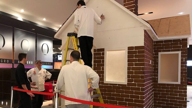 Des hommes travaillent à la construction d’une maison en pain d’épices grandeur nature dans le hall de l’Hôtel Hilton Québec.