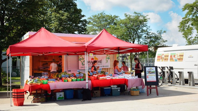 Un marché public en plein air. Deux commis servent deux clientes.