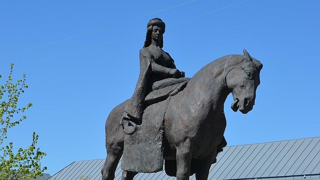 Une femme sur un cheval est montée sur un gros bloc de pierre.