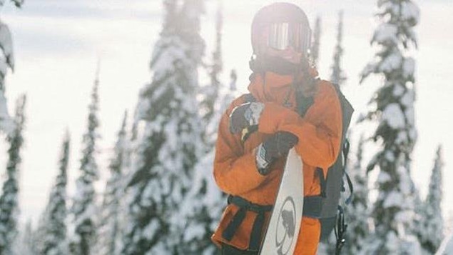 Une femme au sommet des pentes avec sa planche à neige par une journée ensoleillée.
