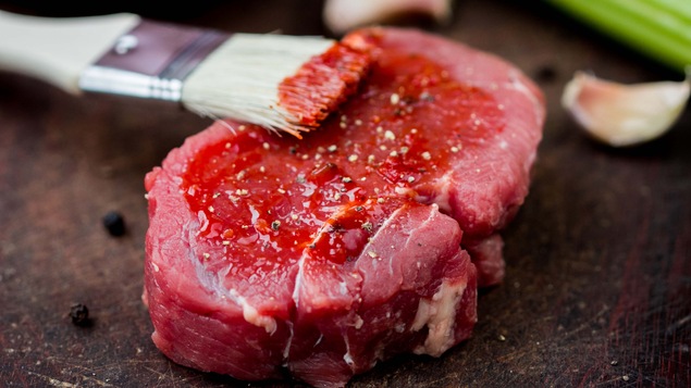 Un pinceau imbibé de marinade est posé sur un morceau de boeuf.