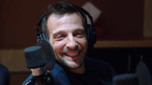 Mathieu Kassovitz, des écouteurs sur la tête, est assis derrière un micro.
