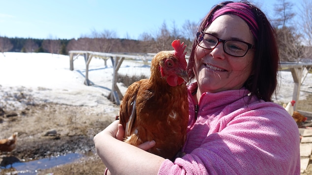 Une femme tient une poule dans ses bras. Derrière eux, on voit un poulailler entouré de neige.
