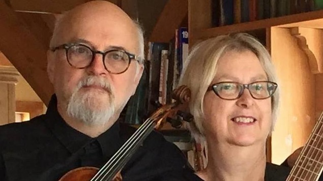 Un homme d'une soixantaine d'années avec des lunettes rondes avec un violon et une femme aux cheveux courts blonds.