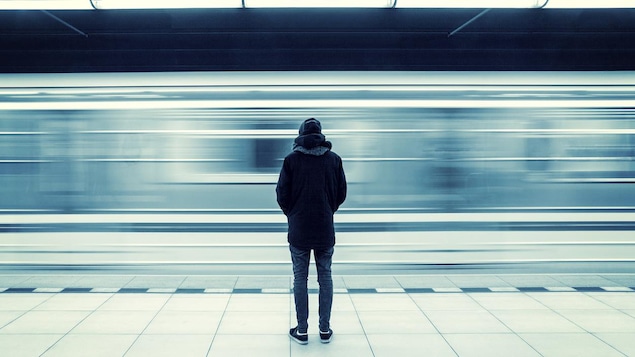 L'homme habillé chaudement est immobile. Il regarde passer le métro, flou.