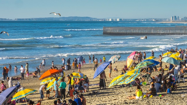 Des touristes sur une plage avec des parasols.